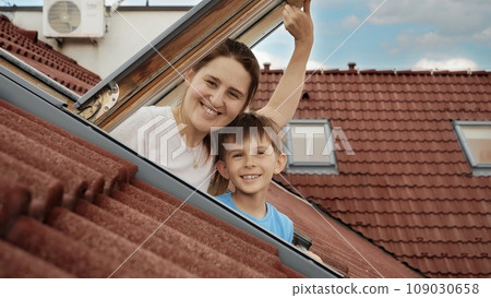Delight of a mother and her son as they open attic windows and enjoy the view outside, illustrating the idea of family joy, parents sharing moments with their kids, and the excitement of relocating to Delight of a mother and her son as they open attic windows and enjoy the view outside, illustrating the idea of family joy, parents sharing moments with their kids, and the excitement of relocating to 109030658