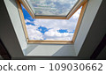 Looking on clouds flying past at the blue sky through open attic window in house roof 109030662
