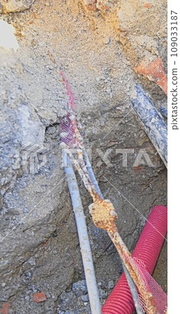 Cables in the trench. High voltage cables in protective red cover in the trench. Concept of electrical installations, construction works, building renovations and building refurbishments. 109033187