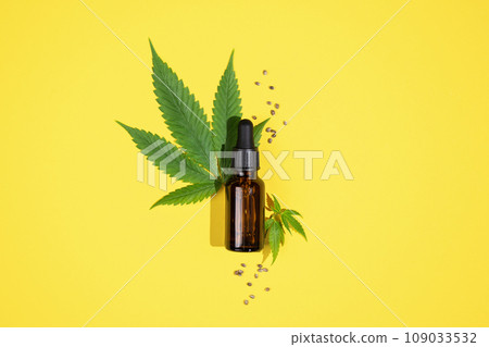 Cannabis oil and hemp leaf on yellow background, flat lay. Hemp CBD oil in a bottle and hemp seeds. Herbal cannabis face serum for skin care. 109033532