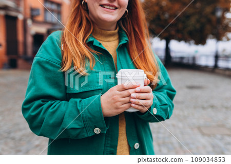 Woman is holding paper coffee cup or tea on urban background. Take away or delivery concept. Copy space. Autumn lifestyle. Place for your text on mug, mockup. Woman is holding paper coffee cup or tea on urban background. Take away or delivery concept. Copy space. Autumn lifestyle. Place for your text on mug, mockup. 109034853