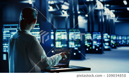 Asian system administrator running code and programming on laptop, troubleshooting and upgrading server farm equipment designed to accommodate mainframes, networking racks and storage arrays Asian system administrator running code and programming on laptop, troubleshooting and upgrading server farm equipment designed to accommodate mainframes, networking racks and storage arrays 109034858