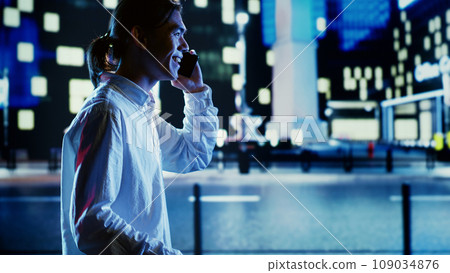 Asian man talking over the phone with wife using cellphone to feel less bored while strolling around dimly illuminated empty avenues at night, blurry cityscape background with bokeh lights Asian man talking over the phone with wife using cellphone to feel less bored while strolling around dimly illuminated empty avenues at night, blurry cityscape background with bokeh lights 109034876