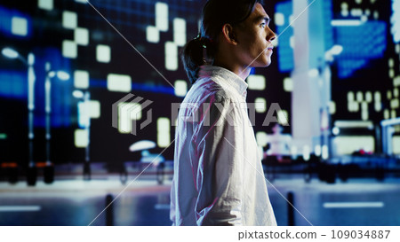 Asian man wandering around city streets at night, looking upwards to surrounding condominiums in metropolitan urban landscape. Joyful businessman leaving work, taking a walk back home Asian man wandering around city streets at night, looking upwards to surrounding condominiums in metropolitan urban landscape. Joyful businessman leaving work, taking a walk back home 109034887