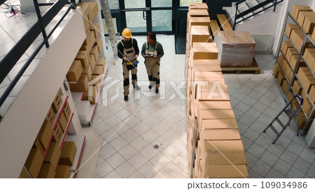 Aerial drone shot of warehouse employees starting shift, inspecting cardboard box parcels before clearing them for shipping. Repository executives making sure stocks and inventory are well organized Aerial drone shot of warehouse employees starting shift, inspecting cardboard box parcels before clearing them for shipping. Repository executives making sure stocks and inventory are well organized 109034986