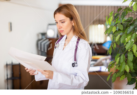 Young female therapist is studying important documents while standing in the office 109036658