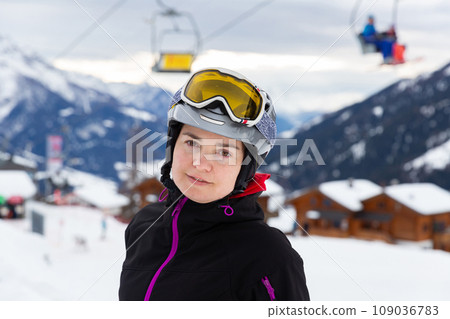 Smiling female skier in helmet and goggles standing on slope 109036783