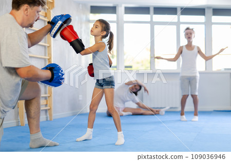 Girl and dad are boxing in gym, father helps child to work out force of blow. Girl and dad are boxing in gym, father helps child to work out force of blow. 109036946