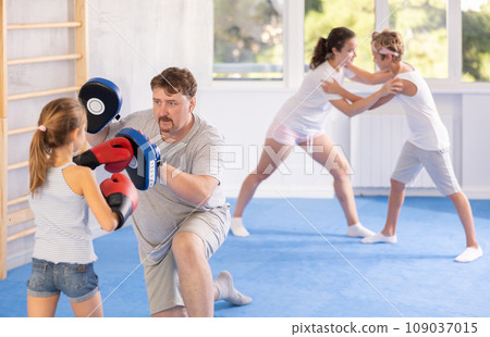 Man holding hitting pads during workout with tween daughter in boxing gloves 109037015