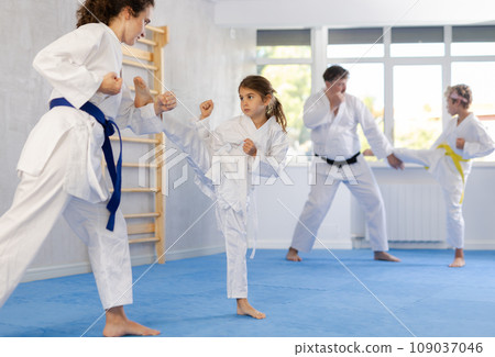 Preteen girl in kimono practicing karate kicks during sparring with mother Preteen girl in kimono practicing karate kicks during sparring with mother 109037046