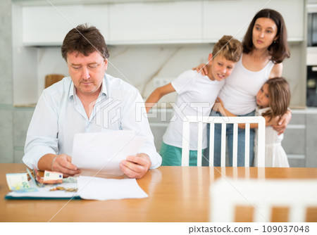 Thoughtful father counting money looking through papers in the kitchen Thoughtful father counting money looking through papers in the kitchen 109037048