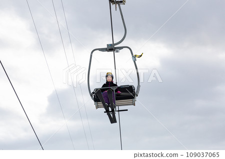 Woman in ski outfit raising on chairlift to slopes for skiing Woman in ski outfit raising on chairlift to slopes for skiing 109037065
