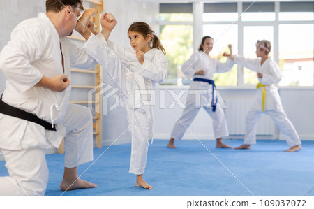 Preteen girl in kimono practicing karate kicks during sparring with father Preteen girl in kimono practicing karate kicks during sparring with father 109037072