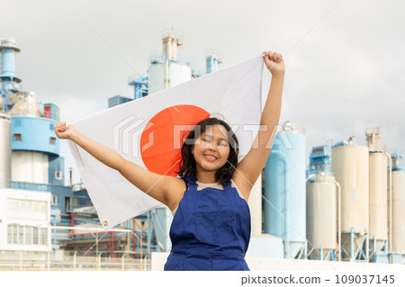 Happy asian girl in work clothes with flag of japan standing in front of industrial scenery Happy asian girl in work clothes with flag of japan standing in front of industrial scenery 109037145