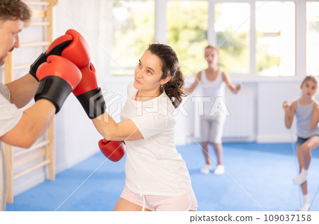 Wife and husband are boxing in gym, man helps female partner to work out force of blow. Wife and husband are boxing in gym, man helps female partner to work out force of blow. 109037158