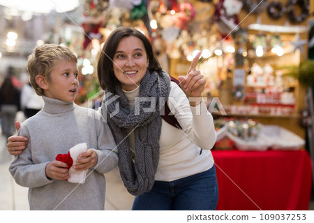 Tween boy with mother choosing Xmas decorations on street fair Tween boy with mother choosing Xmas decorations on street fair 109037253