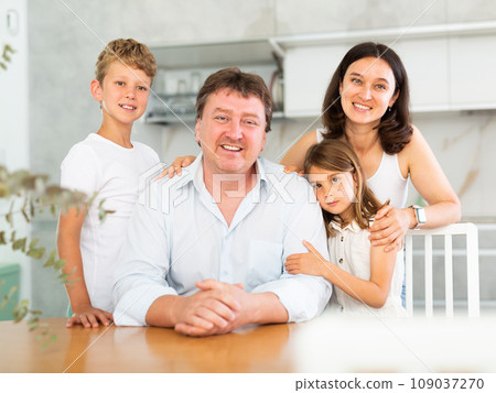 Parents posing with their two little children by the table in the kitchen Parents posing with their two little children by the table in the kitchen 109037270