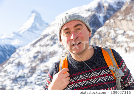 Positive man walking with backpack in mountains on winter day 109037316