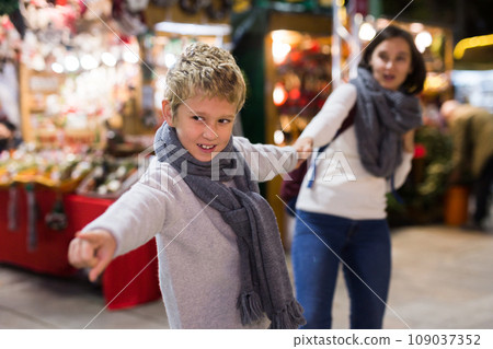 Tween boy pulling mothers hand at festive Christmas fair 109037352