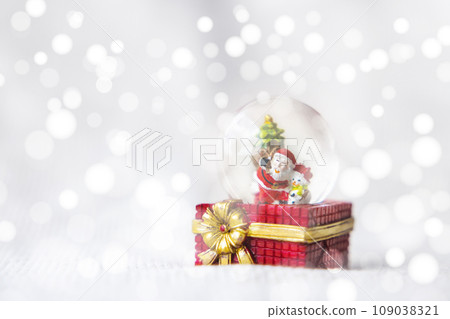 Christmas balls, Santa Claus in a Snow globe, and Pine cones on a Cream-Colored Cloth, set Against a Red Background and exquisite bokeh. New Year Celebration Atmosphere, about of Important day. Christmas balls, Santa Claus in a Snow globe, and Pine cones on a Cream-Colored Cloth, set Against a Red Background and exquisite bokeh. New Year Celebration Atmosphere, about of Important day. 109038321