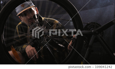 A man in a baseball cap and shirt is repairing a bicycle in a workshop. Bicycle service, sports shop. A mechanic is using a special tool to adjust a bicycle. A man in a baseball cap and shirt is repairing a bicycle in a workshop. Bicycle service, sports shop. A mechanic is using a special tool to adjust a bicycle. 109041242