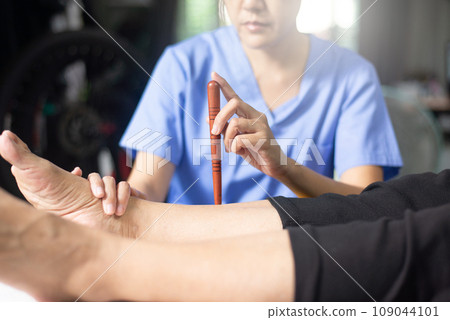 Physiotherapist massaging with wood stick on sick people legs,Reflexology spot thai massage. 109044101