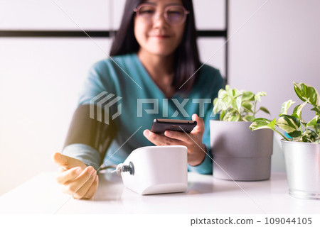 Asian woman holding mobile phone and using blood pressure monitor Asian woman holding mobile phone and using blood pressure monitor 109044105