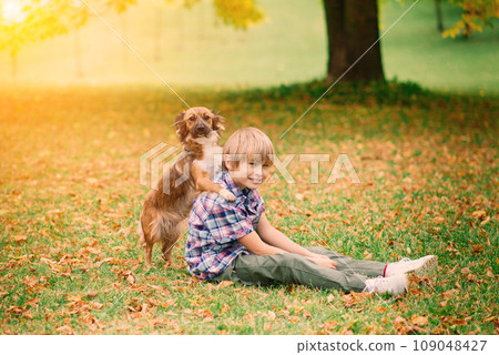 Boy hugging dog and plyaing with in the fall, city park Boy hugging dog and plyaing with in the fall, city park 109048427