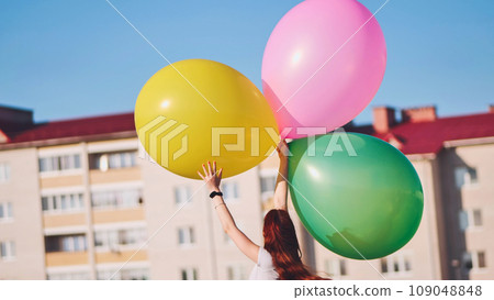 A girl happily poses with large with colorful balloons in the city. A girl happily poses with large with colorful balloons in the city. 109048848