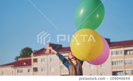 A girl happily poses with large with colorful balloons in the city. A girl happily poses with large with colorful balloons in the city. 109048849