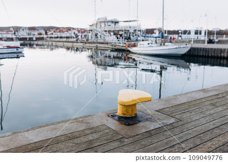yellow bollard, Iron pole for mooring of ships at pier. Landscape with sea wharf. Marina with yacht boats and wooden pier yellow bollard, Iron pole for mooring of ships at pier. Landscape with sea wharf. Marina with yacht boats and wooden pier 109049776