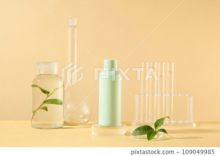 On the beige background, a green bottle unlabeled on glass podium, displayed with green tea leaves and lab equipment. Mockup for design, organic cosmetics, beauty products concept On the beige background, a green bottle unlabeled on glass podium, displayed with green tea leaves and lab equipment. Mockup for design, organic cosmetics, beauty products concept 109049985