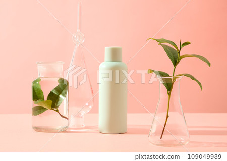 Minimalist creative background for cosmetics or products presentation. Lab equipment containing green tea leaves decorated with green bottle on pink background. Front view, lab theme for advertising 109049989