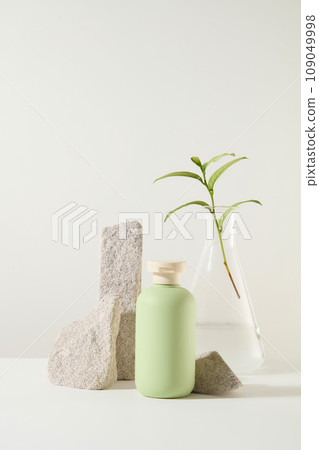 Minimal background for the presentation of products of green tea extract. Green beauty product bottle displayed on white background with gray blocks of stone and green tea leaves 109049998