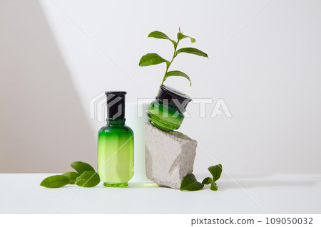 Against a white background, set of cosmetic, bottle and jar displayed on white background with green tea leaves. Minimal scene for advertising, space for design packaging 109050032