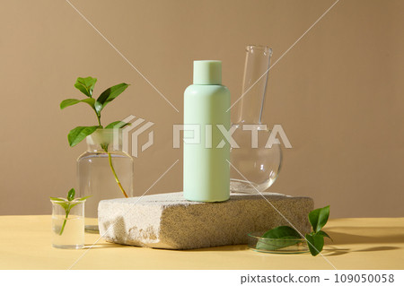 A green bottle on stone decorated with fresh green tea leaves and glass flasks on brown background. Space for design, advertising cosmetic product. Concept for organic cosmetic of green tea extract A green bottle on stone decorated with fresh green tea leaves and glass flasks on brown background. Space for design, advertising cosmetic product. Concept for organic cosmetic of green tea extract 109050058