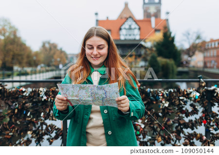 Young pretty 30s woman with backpack holding paper map against the Millers Guild house and the Radunia Canal in Gdansk, Vacation concept. Happy Woman Searching locations at autumn day 109050144