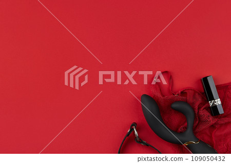 Black vibrator with a black leather choker, lipstick and erotic red lingerie on the red background 109050432