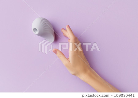 Female hand with pink polish nails is touching a purple clitoral vibrator on the purple background 109050441