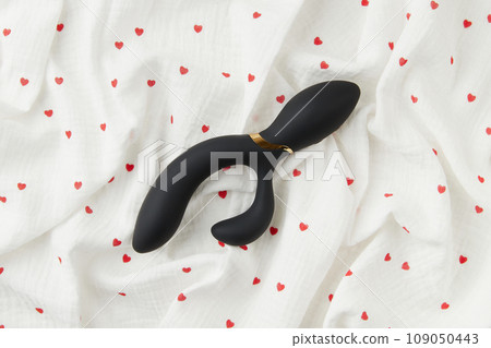 Black vibrator on the white crumpled fabric with heart print. Sex toys for adults. Flat lay, top view Black vibrator on the white crumpled fabric with heart print. Sex toys for adults. Flat lay, top view 109050443