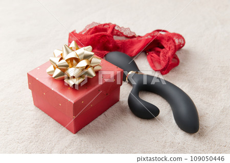 Black vibrator, red lingerie and red gift box with golden bow on the white fur background 109050446