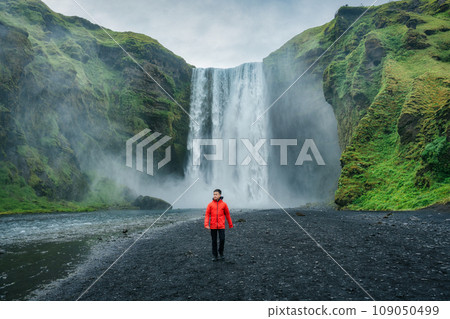 Powerful Skogafoss waterfall and male tourist walking in summer at Iceland 109050499