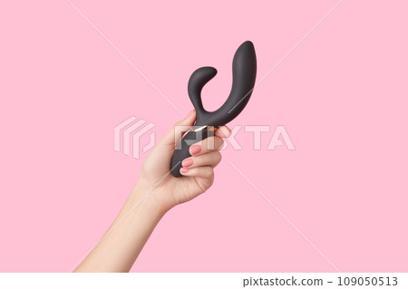 Female hand with pink polish nails is holding a black vibrator on the pink background 109050513