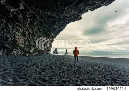 Reynisdrangar natural rock formation with female tourist standing in halsanefshellir cave on black sand beach in summer at Iceland 109050514