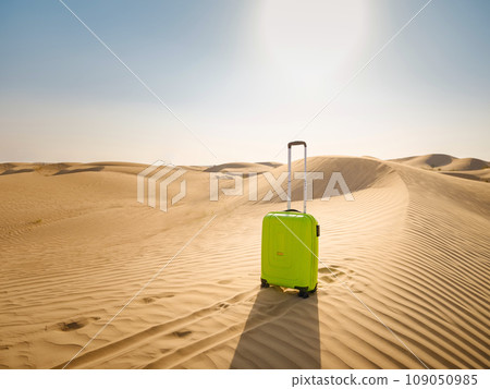 bright light green or yellow suitcase in sands of desert dunes. Concept and idea of travel to United Arab Emirates, Dubai sands at sunset. Summer holiday travel concept bright light green or yellow suitcase in sands of desert dunes. Concept and idea of travel to United Arab Emirates, Dubai sands at sunset. Summer holiday travel concept 109050985