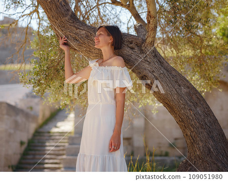 Beautiful Asian young woman in white dress outdoor near olive tree. embracing fresh air and engaging in outdoor activities. Friluftsliv concept means spending as much time outdoors as possible 109051980
