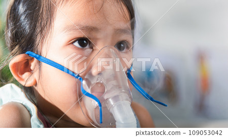 Kid girl making makes inhalation nebulizer steam sick cough at home, Asian Child using nebulizer mask equipment alone have smoke, stuffy nose and runny, oxygen spray inhaler therapy, Health medical 109053042