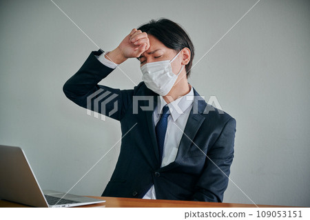 A young male office worker who has a headache and puts his hand on his forehead 109053151