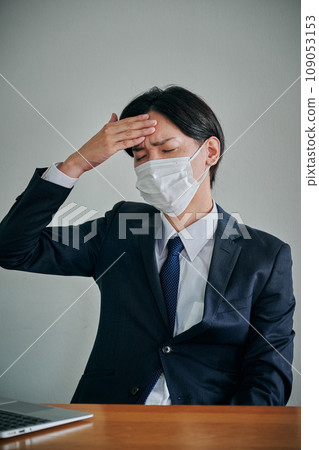 A young male office worker who has a headache and puts his hand on his forehead 109053153