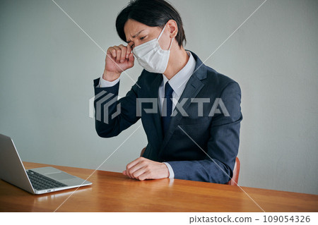 A young male office worker has itchy eyes and rubs them with his fingers A young male office worker has itchy eyes and rubs them with his fingers 109054326